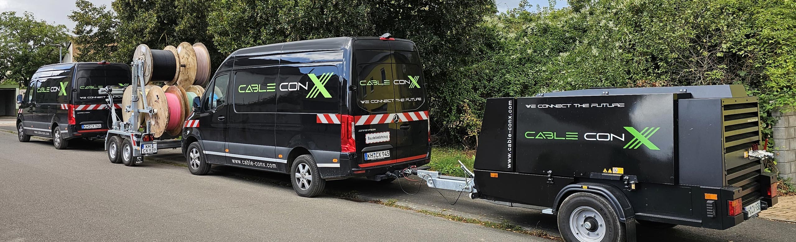 Zwei schwarze Firmenfahrzeuge mit Logo Cable conX und Anhängern am Staßenrand. Einmal Kabeltrommelanhänger und einmal ein Kompressor.